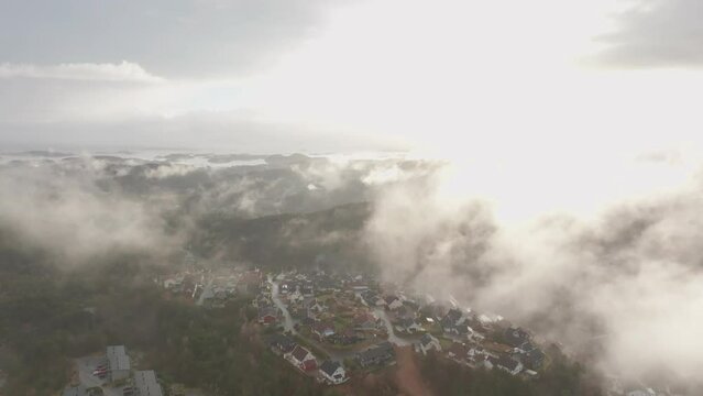 Drone footage of housing estate in Norway with some fog floating in th air and sun lighting up the clouds