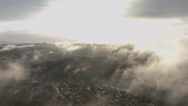 Drone footage of housing estate in Norway with some fog floating in th air and sun lighting up the clouds
