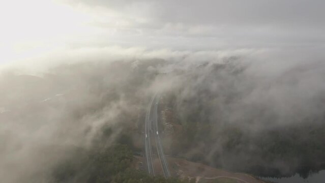 Drone footage of highway, and housing estate in Norway with some fog floating in the air and sun lighting up the clouds