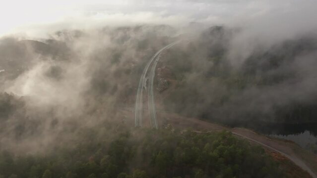 Drone footage of highway, and housing estate in Norway with some fog floating in the air and sun lighting up the clouds
