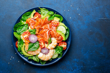 Salmon salad for ketogenic diet with shrimp, avocado, spinach, cucumber, tomato, cashew nuts, sesame. Low-carbohydrate lunch rich in healthy fats. Blue table background, top view