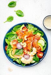 Ketogenic diet salad with salmon, shrimp, avocado, spinach, cucumber, tomato, cashew nuts, sesame. Low-carbohydrate lunch rich in healthy fats. White table background, top view