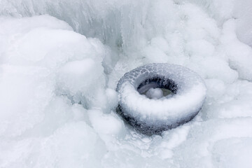 A discarded tire from a car is frozen into ice after freezing rain in winter. After the rain everything was covered with snow.