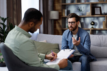 Visit to a psychologist. A man sits on a couch and talks to a psychotherapist. The patient is...