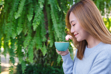 Portrait image of a beautiful young asian woman holding and drinking hot coffee in the outdoors