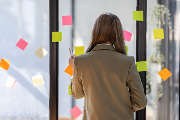 Business female employee with many conflicting priorities arranging sticky notes commenting and...