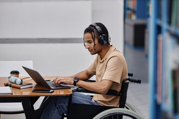 Black teenage boy with disability studying in college library and using laptop