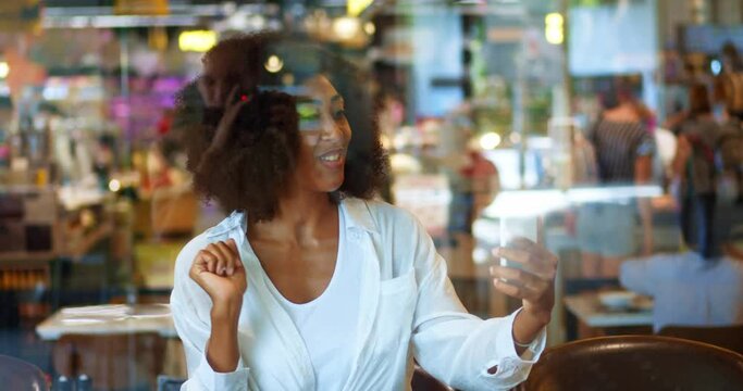 African American positive young woman, smiling cheerfully to her interlocutor while chatting talking online in cafe using her smartphone and mobile video chat application. Video call, chat, conference