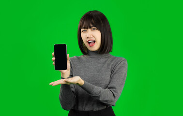 Young Asian woman showing a Smartphone with blank screen on green screen. Great Mobile Offer. 