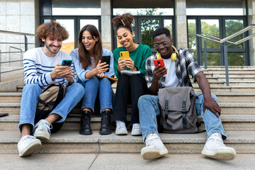 Multiracial college student friends look mobile phone laughing together. University students using...