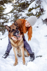 A cute dog sits at the feet of the owner in the winter forest. Traveling with a pet, a faithful companion. Adorable german shepherd dog traveling with young hipster woman in winter forest. 