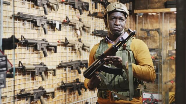 African american guy in military equipment with weapon in army shop