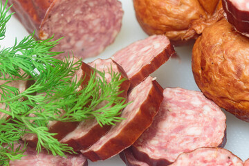 two types of sausages on a white cutting board with a green sprig of dill, macro