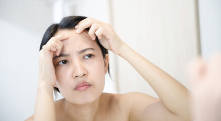 Problem skin. Concerned young asian women popping pimple on cheek while standing near mirror in bathroom. young asian women with acne