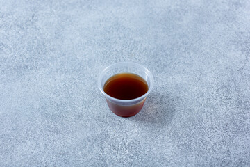 A view of a plastic condiment cup of a brown colored sauce.