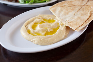 A view of a plate of hummus, with some pieces of pita bread.