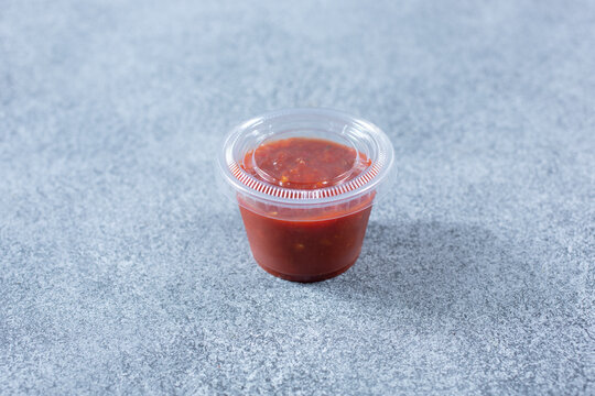 A View Of A Closed Plastic Condiment Cup Of Red Garlic Chili Sauce.