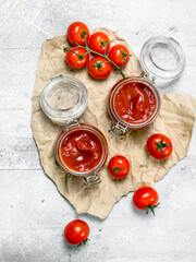 Tomato sauce in a glass jar on paper and cherry.