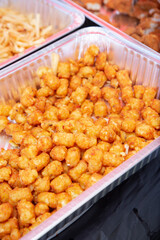 A view of a large aluminum foil container full of deep fried tater tots.