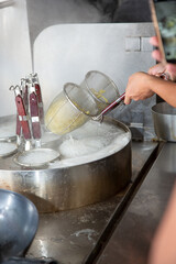 A view of a hand using ramen noodle strainers.