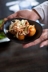 A view of hands holding a plate of takoyaki.