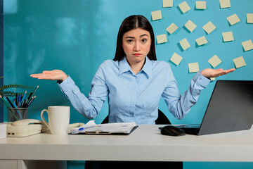 Female employee sitting in modern office making dont know gesture to camera, feeling hesitant and...