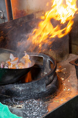 A view of a wok filled with food, flipped and tossed with flames from the stove, seen at a local restaurant kitchen.