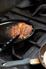 A view of a flat skillet cooking a slice of marinated beef, seen at a local restaurant kitchen.