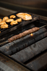 A view of several pieces of meat cooking on a griddle surface, in a restaurant setting.