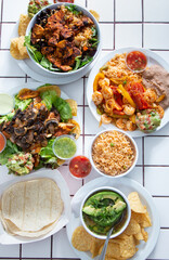 A top down view of several Tex-Mex entrees on a tile table surface.