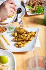 A view of a hand holding a fork over a plate of chicken satay.
