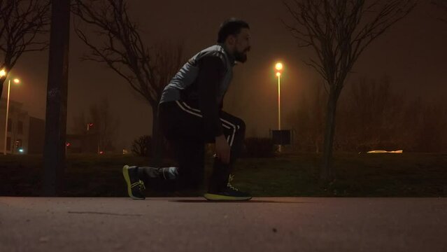 Runner ties his shoelaces in a spots track at night time.
