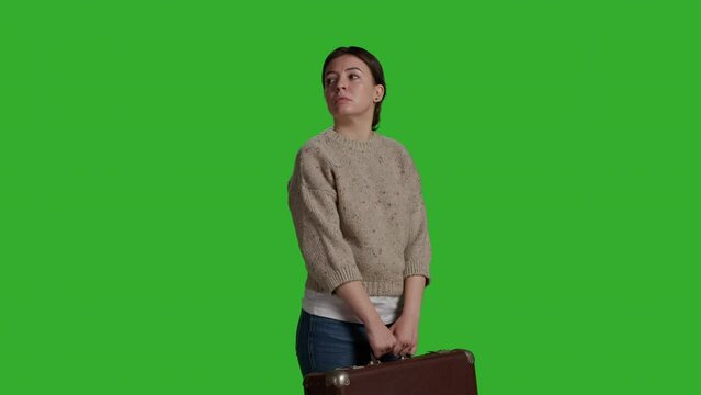 Side view of model carrying vintage suitcase in front of camera, holding briefcase before leaving on journey. Cheerful woman acting optimistic and having travel bags or luggage over greenscreen.