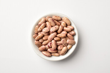 Uncooked pinto beans in bowl on white background - obrazy, fototapety, plakaty