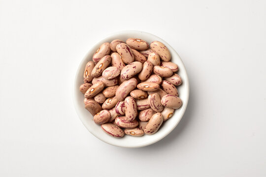 Uncooked pinto beans in bowl on white background