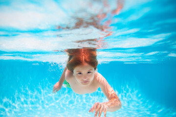 Fototapeta na wymiar Child swimming underwater in swimming pool. Funny kids boy play and swim in the sea water. Kids swim on summer vacation.