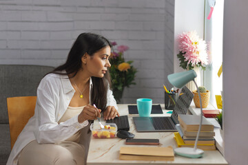 Portrait of a young woman eating fruit while working at home office