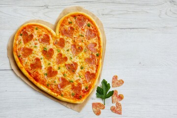 Heart shaped pizza with heart shaped salami on parchment paper with white wood background.Creative...