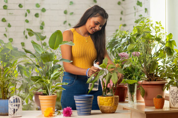 Young woman spraying water on plants while gardening at home
