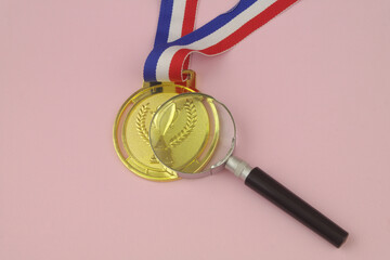 Review achievements in sport concept. Golden medal under magnifying glass on pink background. 