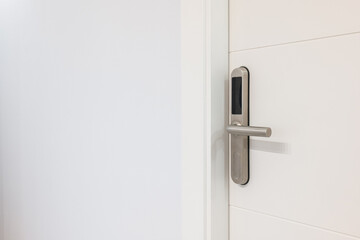 Closeup of an entrance white door with an electronic mortise lock. An electronic unit with display is built into metal handle. Opening doors with plastic card with microchip or digital code.