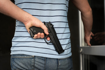 an armed criminal with a dhrt pistol enters the premises. Attempted robbery. Crime concept. bank robbery. self-defense with firearms. the man hides the gun behind his back. © diy13