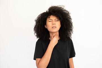 Fototapeta na wymiar Portrait of unwell young woman suffering from angina. Biracial lady with afro hairstyle wearing black T-shirt standing with closed eyes and touching throat. Diseases concept