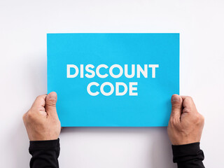 Discount code offered to customers as a purchasing incentive that reduces the price of an order. Male hand holding a blue paper with the message discount code.