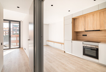 Empty contemporary kitchen, living room and bedroom with balcony at refurbished apartment. Wooden furniture and modern appliances