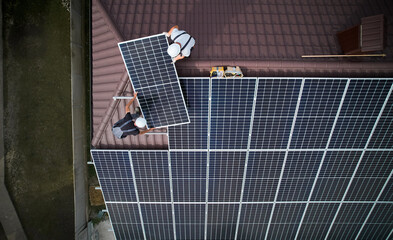 Men technicians mounting photovoltaic solar moduls on roof of house. Workmen in helmets installing...