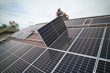 Man technician mounting photovoltaic solar moduls on roof of house. Mounter in helmet installing...
