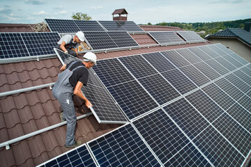 Men technicians mounting photovoltaic solar moduls on roof of house. Engineers in helmet installing...