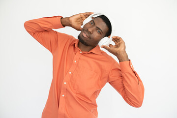 Portrait of happy young man listening to music in headphones over white background. African American guy wearing orange shirt looking at camera and smiling. Music and leisure concept