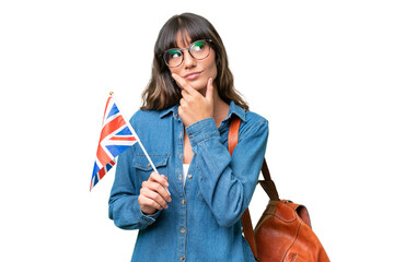 Young caucasian woman holding an United Kingdom flag over isolated background having doubts